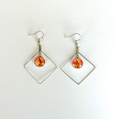 A pair of stainless steel statement earrings, with wiring in the shape of a diamond and a charm with Lilia Munn's art in the center