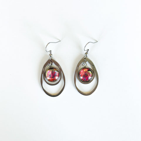 A pair of stainless steel statement earrings, with steel in the shape of a clam or oyster and a charm with Lilia Munn's art in the center.