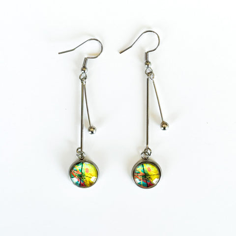 A pair of stainless steel statement earrings, with two stainless steel rods dangling, one of which contains a charm with Lilia Munn's art.